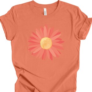Puede incluir: Una camiseta naranja coral con un gr&aacute;fico de margarita rosa y naranja.