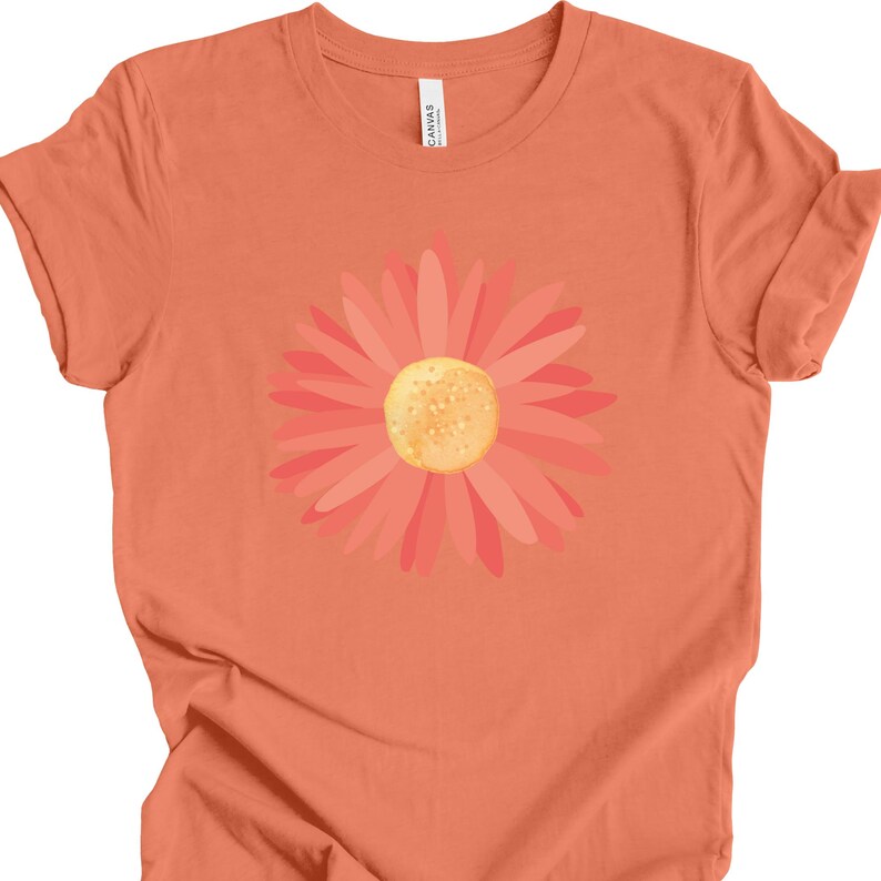 Puede incluir: Una camiseta naranja coral con un gr&aacute;fico de margarita rosa y naranja.