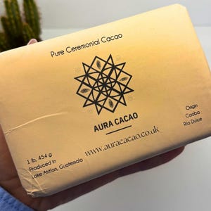 以下が含まれることがあります： 「Pure Ceremonial Cacao」の文字が上部に書かれた、Aura Cacaoの長方形のパッケージ。幾何学模様のデザインとブランド名「AURA CACAO」が特徴です。重量は454gで、グアテマラのLake Atitlanで製造されています。