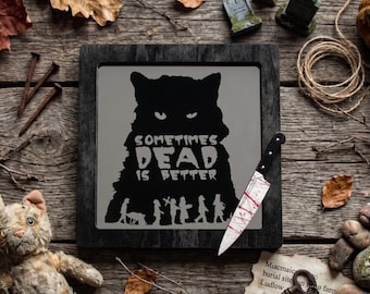 May include: A framed black and white image with the text "SOMETIMES DEAD IS BETTER" and a silhouette of a cat. A bloody knife rests beside the frame. The image is surrounded by Halloween-themed decorations, including a stuffed cat and autumn leaves.