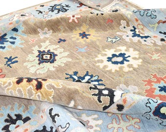 Könnte beinhalten: Ein aufgerollter Teppich mit einem beigefarbenen Mittelfeld und einem hellblauen Rand. Der Teppich weist ein sich wiederholendes Muster aus floralen und geometrischen Designs in Blau-, Orange- und Weißtönen auf. Die Textur des Teppichs ist sichtbar.