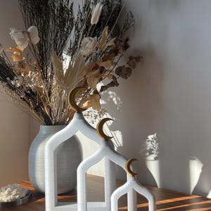 Puede incluir: Tres estructuras decorativas blancas con tapas de media luna dorada. Las estructuras están en tamaño decreciente y están dispuestas de izquierda a derecha. Las estructuras recuerdan a una mezquita.