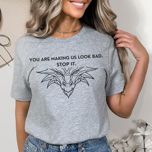 May include: Gray t-shirt with a black dragon graphic and the text "You are making us look bad. Stop it."