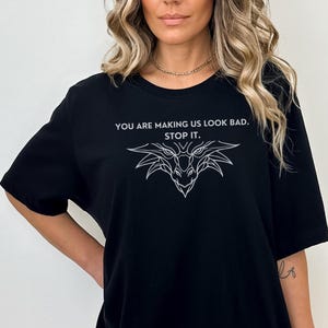 May include: Black t-shirt with a white graphic of a dragon's head and the text "You are making us look bad. Stop it."