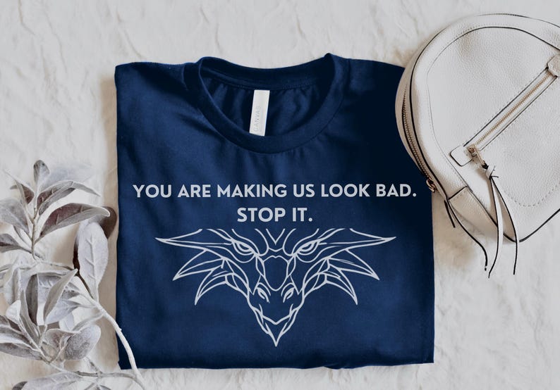 May include: A navy blue t-shirt with a white dragon graphic and the text "You are making us look bad. Stop it."