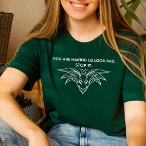 May include: A green t-shirt with a white dragon graphic and the text "You are making us look bad. Stop it."