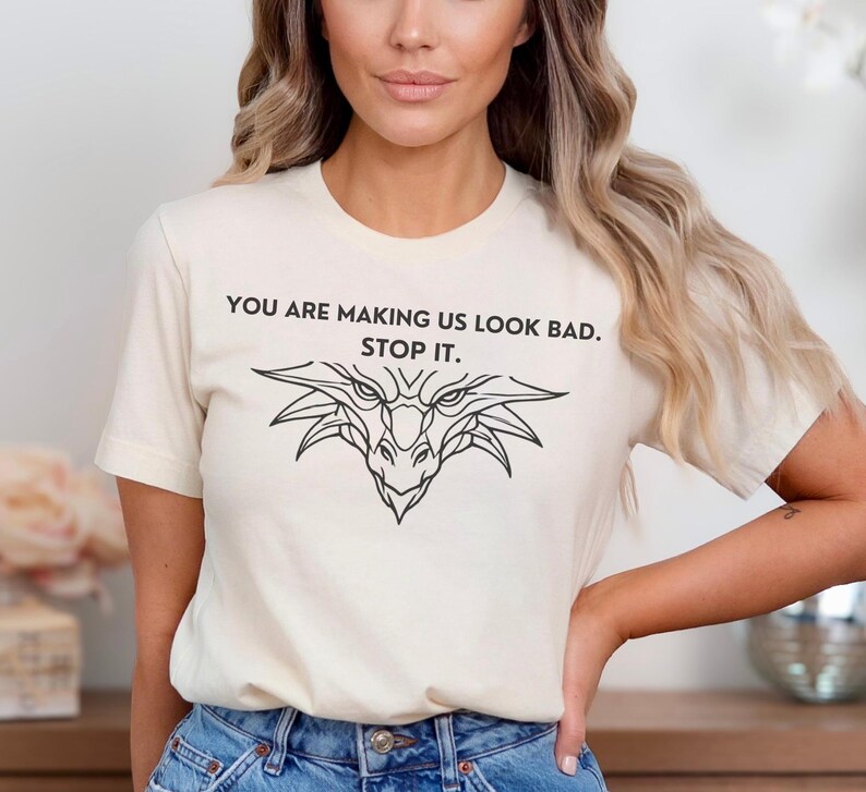 May include: A white t-shirt with a black dragon graphic and the text "You are making us look bad. Stop it."