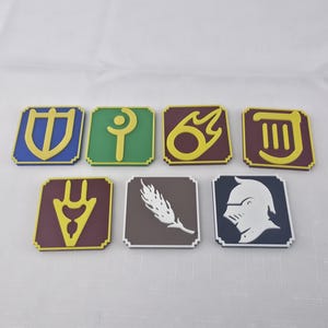 May include: Set of eight square, colorful coasters featuring various symbols. Each coaster has a colored border and a unique design in the center, including a shield, a crescent, and a knight's helmet. The coasters are arranged on a white surface.
