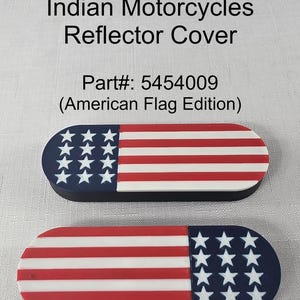 Puede incluir: Dos reflectores de motocicleta con un diseño de bandera estadounidense. Cada cubierta tiene forma ovalada alargada con una sección azul con estrellas blancas y rayas rojas y blancas. El texto "Indian Motorcycles Reflector Cover" está en la parte superior.