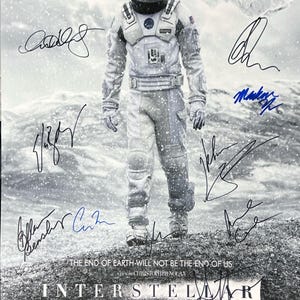 May include: A black and white movie poster for the film Interstellar, featuring a man in a spacesuit walking on a snowy landscape. The poster includes the film's title, the tagline "The end of earth will not be the end of us." and the names of the actors Matthew McConaughey, Anne Hathaway, Jessica Chastain, and Michael Caine. The poster is signed by all four actors.