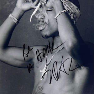 May include: Black and white photograph of a person exhaling smoke from a lit cigarette. The person is wearing a bandana, a cross necklace, and a bracelet. The image includes signatures and tattoos.
