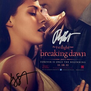 Puede incluir: Póster de la película "Amanecer - Parte 1" de la saga Crepúsculo, con dos personas abrazándose. El póster incluye el título de la película, la fecha de estreno y firmas.