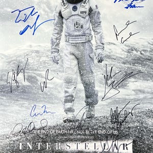 May include: A black and white movie poster for the film Interstellar, featuring Matthew McConaughey in a spacesuit standing on a snowy landscape. The poster includes the film's title, tagline, and cast and crew credits. The poster is signed by the cast members, including Matthew McConaughey, Anne Hathaway, Jessica Chastain, and Michael Caine.