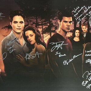Puede incluir: Un póster promocional con un grupo de actores de la serie de películas Crepúsculo. El póster incluye firmas y citas manuscritas. El fondo muestra una escena de bosque. Los actores visten diferentes atuendos.