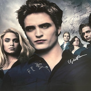 Puede incluir: Un póster firmado con el reparto de la saga Crepúsculo. El póster presenta a Robert Pattinson, Kristen Stewart, Taylor Lautner, Ashley Greene y Jackson Rathbone. El póster está firmado por los miembros del reparto con sus nombres en marcador negro.