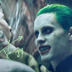 May include: A close-up of two figures from a film. One figure has green hair, pale skin, and metal braces. The other figure has a painted smile on their face. The text "TJ!" is written in green.