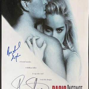 May include: A movie poster for the film "Basic Instinct" starring Michael Douglas and Sharon Stone. The poster features a close-up of the two actors, with Stone's face partially obscured by Douglas's shoulder. The poster is signed by both actors.