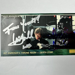 Pode incluir: Um cartão colecionável de "Return of the Jedi" com Luke Skywalker e Darth Vader na sala do trono do Imperador. O cartão tem autógrafos e o texto "INT. EMPEROR'S THRONE ROOM - DEATH STAR". O cartão tem uma borda verde.