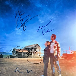 May include: A movie poster featuring two people looking up at a starry sky. A house and truck are in the background. The poster has several signatures in black ink.