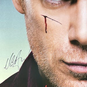 Puede incluir: Primer plano del rostro de un hombre con un pequeño corte y sangre. La palabra "DEXTER" está impresa en rojo en la parte inferior. Una firma está visible en la esquina superior izquierda. La imagen es un artículo promocional para la serie de televisión.