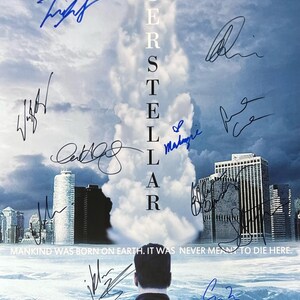 May include: A movie poster for the film "Interstellar" featuring a rocket launching into a cloudy sky. The poster is signed by the cast and crew, including Matthew McConaughey, Anne Hathaway, Jessica Chastain, and Christopher Nolan.