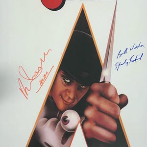 May include: A vintage movie poster for Stanley Kubrick's A Clockwork Orange. The poster features a black and white image of Alex, the main character, holding a knife. The poster is signed by Stanley Kubrick and Malcolm McDowell. The text on the poster reads "Stanley Kubrick's A Clockwork Orange" and "Based on the novel by Anthony Burgess."