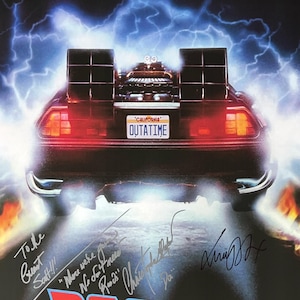 May include: A movie poster for the film "Back to the Future" featuring a DeLorean time machine with a license plate that reads "OUTATIME". The poster is signed by the cast members: Michael J. Fox, Christopher Lloyd, Lea Thompson, and Thomas F. Wilson. The poster also includes the date "NOV 05 1955" and the time "01:21 PM".