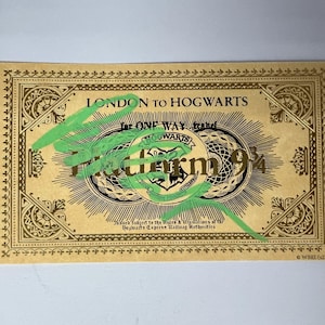 Könnte beinhalten: Ein goldenes Ticket mit dem Text "London to Hogwarts" und "Platform 9 3/4". Das Ticket hat einen verzierten Rand und ein Hogwarts-Wappen in der Mitte. Grüne Markierungen verdecken einen Teil des Textes.