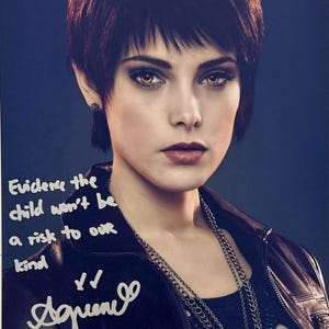Puede incluir: Retrato de una persona con pelo corto y oscuro y ojos marrones, con una chaqueta de cuero negra y un collar de cadena plateada. La imagen incluye texto manuscrito que dice "Evidence the child won't be a risk to our kind" y una firma.