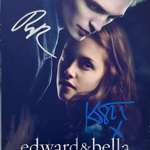 Puede incluir: Póster de la película Crepúsculo con Edward y Bella, con firmas y graffiti azul. El título "edward & bella" se muestra debajo de los rostros de los actores, con "twilight" debajo.