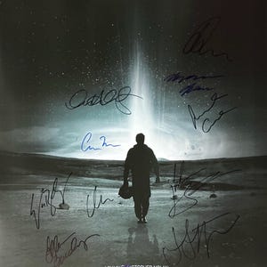 May include: Movie poster for the film Interstellar, featuring Matthew McConaughey. The poster shows a silhouetted figure walking towards a bright light, with several signatures and the film's title. The release date is November 2014.
