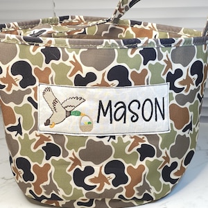 May include: A camouflage fabric tote bag with a duck and basket design and the name "Mason" embroidered on it.