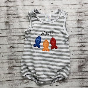 May include: Gray and white striped baby onesie with a personalized name "Wyatt" embroidered on the front. Three colorful fish are embroidered below the name.