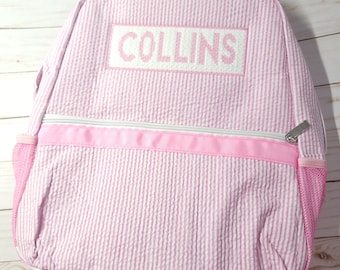 May include: Pink and white striped backpack with a pink zipper and a white embroidered name tag that says "COLLINS".
