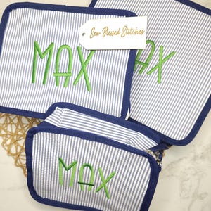 Puede incluir: Tres artículos a juego con un estampado de rayas azules y blancas. Los artículos están ribeteados en azul marino y bordados con el nombre "MAX" en verde. Una etiqueta dice "Sew Blessed Stitches".