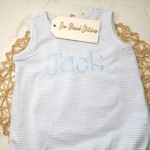 May include: A light blue and white striped baby romper with the name "Jack" embroidered in light blue. The romper has a tag that says "Sew Blessed Stitches". The romper is sleeveless.