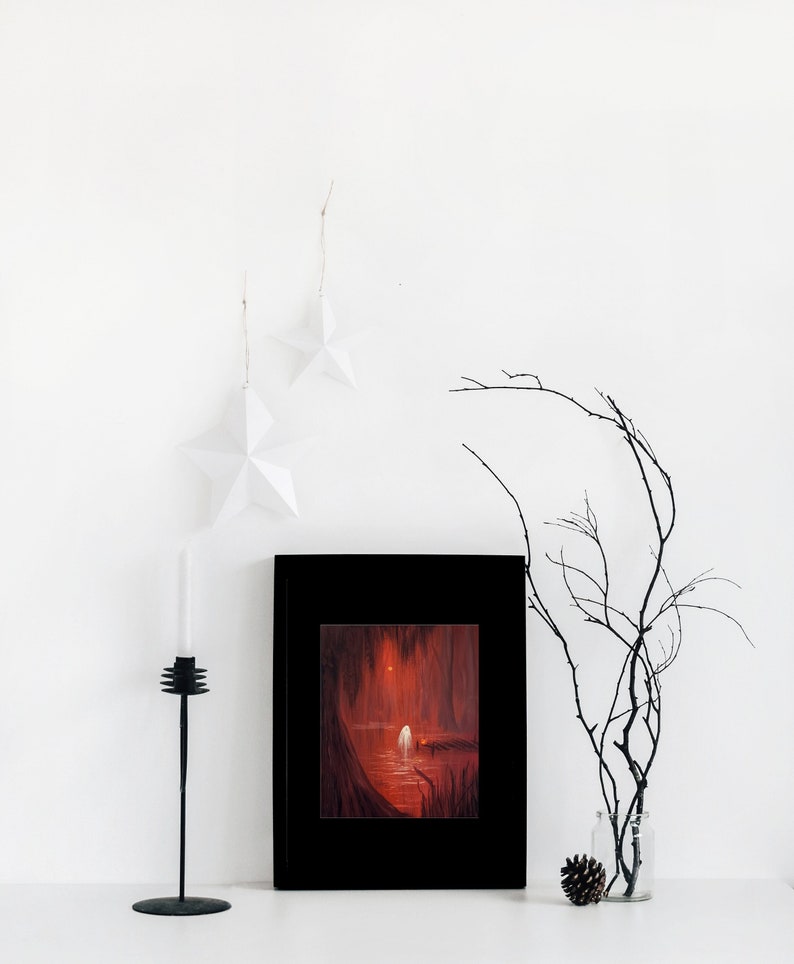 May include: A framed painting of a dark, red forest scene with a white figure standing on a wooden dock. The figure is surrounded by trees and water. The painting is in a black frame and is hanging on a white wall.