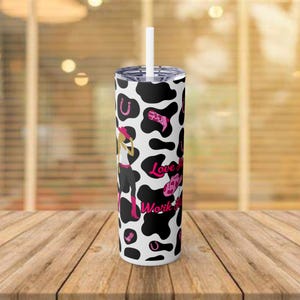 Könnte beinhalten: Ein schwarz-weißer Becher mit Kuhmuster und einem pinkfarbenen Cowgirl-Design sowie dem Text "Love My Work"