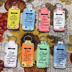 May include: A collection of eight keychains with various floral and scripture designs. Each keychain features a rectangular shape with a metal ring and a black slot. The keychains display inspirational quotes in different colors.