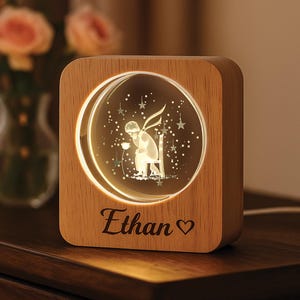 May include: A wooden night light with a circular illuminated design featuring a seated figure, stars, and a flower. The name "Ethan" is engraved below the design, with a heart symbol. The light has a warm glow.