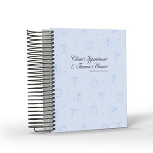 May include: A light blue spiral-bound planner with a black wire coil. The cover features a repeating pattern of small blue line-art icons including alarm clocks, money bags, and bows. The text reads Client Appointment & Finance Planner.