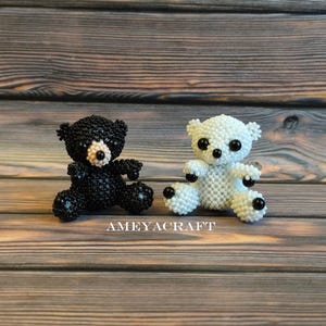 Könnte beinhalten: Zwei kleine Bärenfiguren aus winzigen Perlen. Ein Bär ist komplett schwarz mit einer hellen Schnauze, während der andere komplett weiß ist. Beide Bären haben runde schwarze Perlenaugen sowie schwarze Perlenakzente an Pfoten und Ohren.
