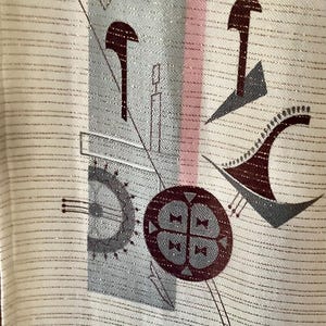 May include: Cream fabric with an abstract pattern and silver threads. The design incorporates geometric shapes in grey, burgundy, and pink, including circles, lines, and stylized forms. The fabric has a subtle striped texture.