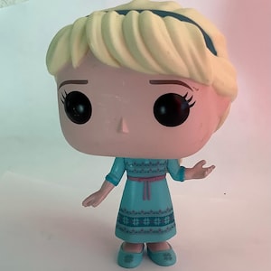 May include: A Funko Pop! vinyl figure of Elsa from Disney's Frozen. The figure features a light blue dress with a pink belt, blonde hair, and large black eyes. The figure is approximately 4 inches tall.