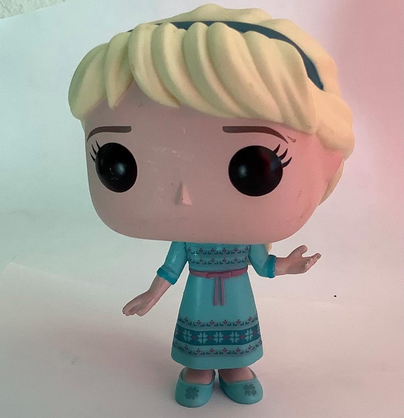 May include: A Funko Pop! vinyl figure of Elsa from Disney's Frozen. The figure features a light blue dress with a pink belt, blonde hair, and large black eyes. The figure is approximately 4 inches tall.