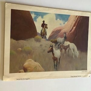 May include: A vintage print featuring a rider on horseback among a herd of horses in a desert canyon. The text reads Santa Fe Dining Car, Fred Harvey Service, and Navajo Ponies. The scene includes red rock formations, blue sky, and clouds.