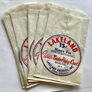 Puede incluir: Un montón de bolsas de papel vintage con una etiqueta circular roja, blanca y azul que dice "LAKELAND Mince Pie". La etiqueta también indica "With Tender Flaky Crust" y "Net Wt. 4 oz."