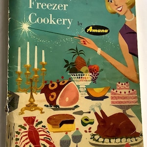 May include: Vintage cookbook cover titled "Basic Freezer Cookery" by Amana. The illustration features a woman in a purple dress pointing a magic wand at a table laden with food, including a ham, turkey, cake, and lobster. The background is teal.