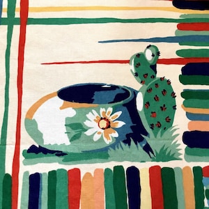Op de afbeelding: Een textielstof met een crèmekleurige achtergrond en een centrale illustratie van een blauwe kom met een witte bloem, geplaatst naast een groene cactus. Het ontwerp bevat horizontale en verticale strepen in rood, groen, blauw en geel.