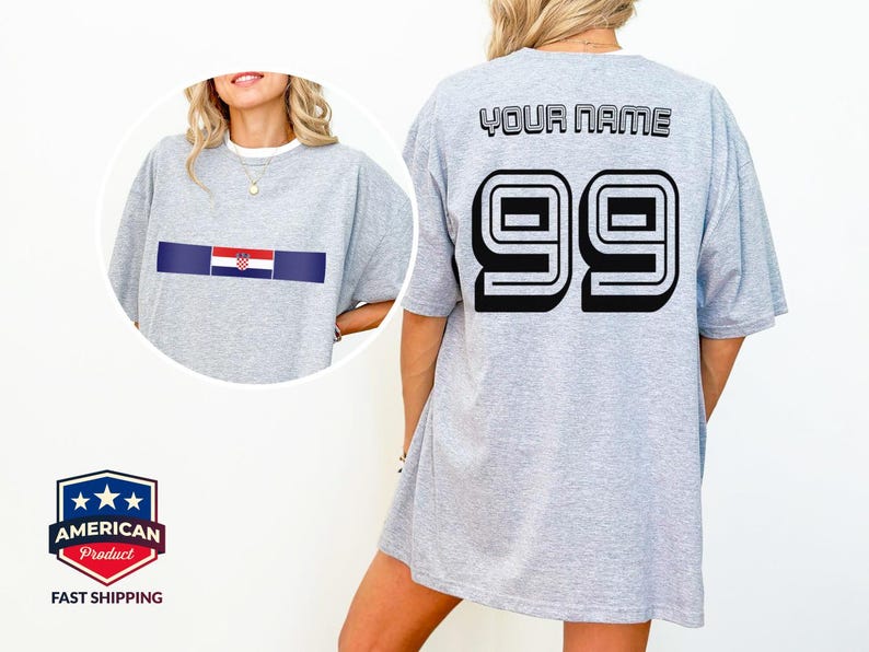 May include: A light gray t-shirt featuring a horizontal stripe with the Croatian flag on the front. The back displays the text YOUR NAME in black block letters above the large black number 99 with a white outline and a black drop shadow.